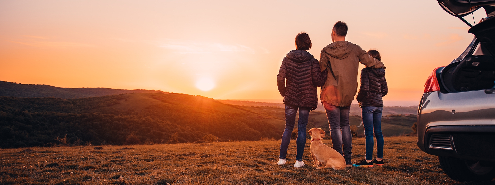 Family with dog embracing at hill and looking at sunset